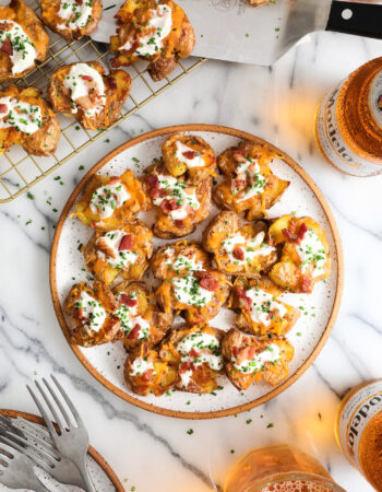 white plate filled with loaded smashed potatoes and surrounded by a few beer bottles