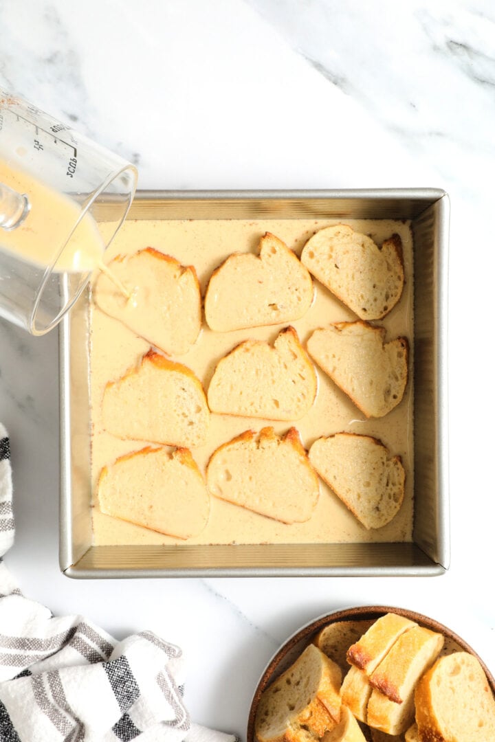 a square pan filled with French toast crostini that has been soaked in egg wash and is waiting to be fried.