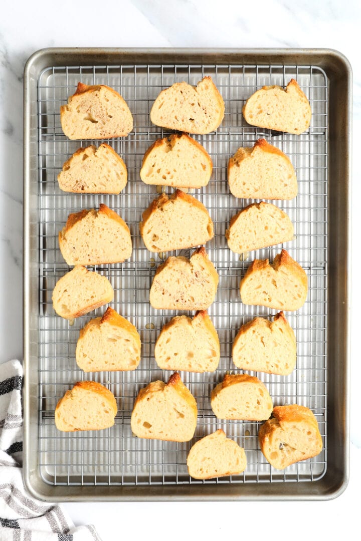 a cooling rack filled with French toast crostini that has been soaked in egg wash and is waiting to be fried.