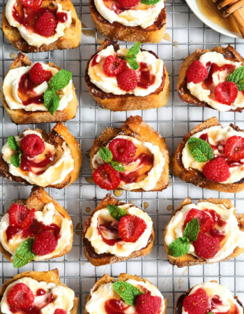 a cooling rack filled with French toast crostini and topped with ricotta, raspberry jam and mint leaves