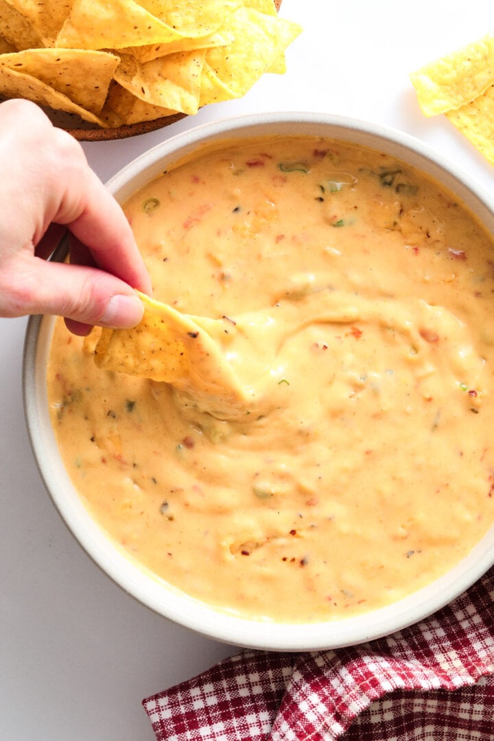 gray bowl of queso dip with chips and a red checkered napkin on the side.