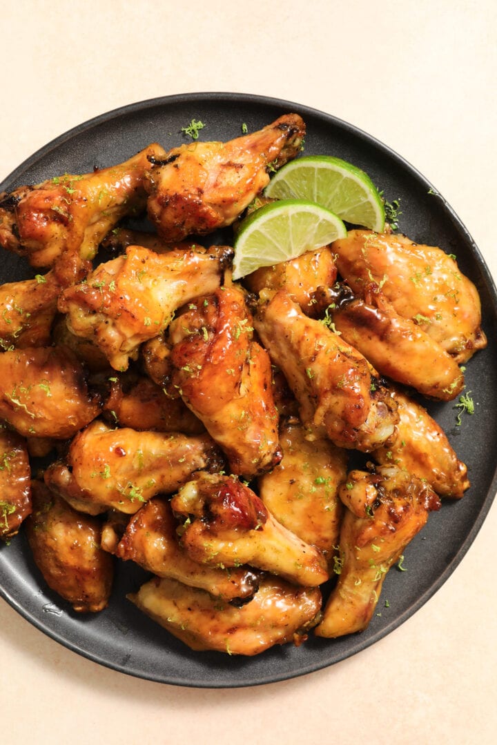 dark gray plate of chicken wings, garnished with lime slices and lime zest.
