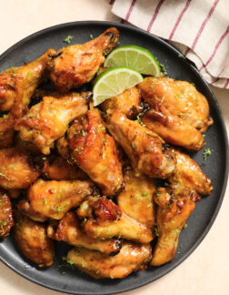 dark gray plate of chicken wings, garnished with lime slices and lime zest.