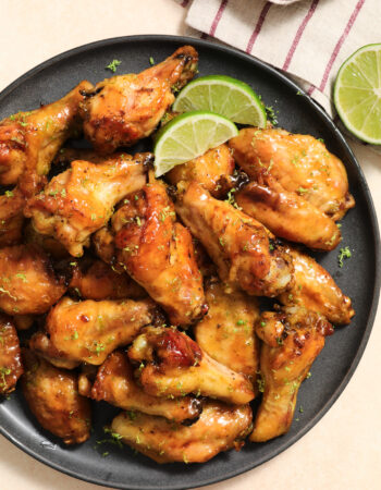 dark gray plate of chicken wings, garnished with lime slices and lime zest with a striped napkin in the upper right hand corner.