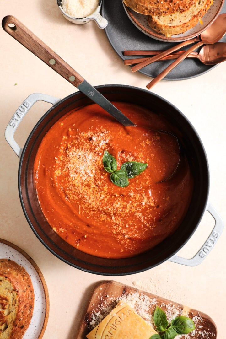 large pot of tomato soup that is garnished with parmesan cheese and fresh basil. There is a cutting board with a block of parmesan at the bottom of the photo.