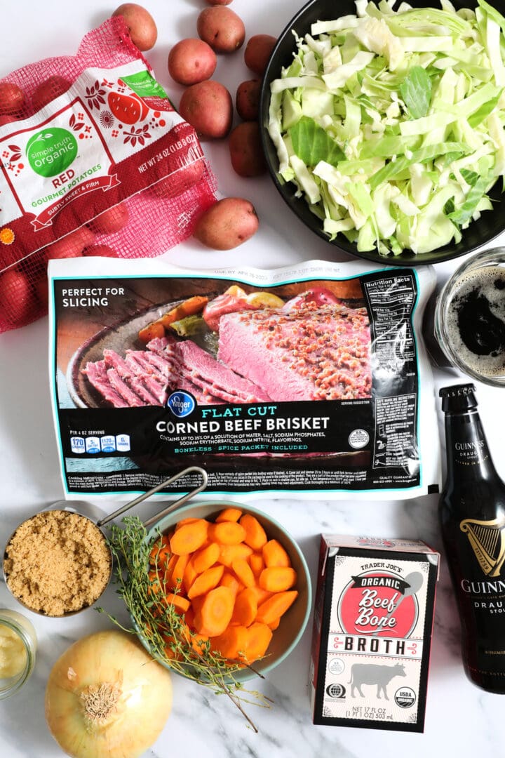 ingredients to make corned beef and vegetables, including beef stock, beer, cabbage, potatoes, carrots, fresh thyme, onion, brown sugar and garlic.