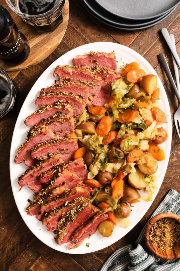 white platter with slices of corned beef brisket and vegetables, including cabbage, carrots and potatoes.