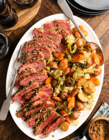 white platter with slices of corned beef brisket and vegetables, including cabbage, carrots and potatoes.