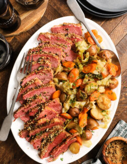 white platter with slices of corned beef brisket and vegetables, including cabbage, carrots and potatoes.