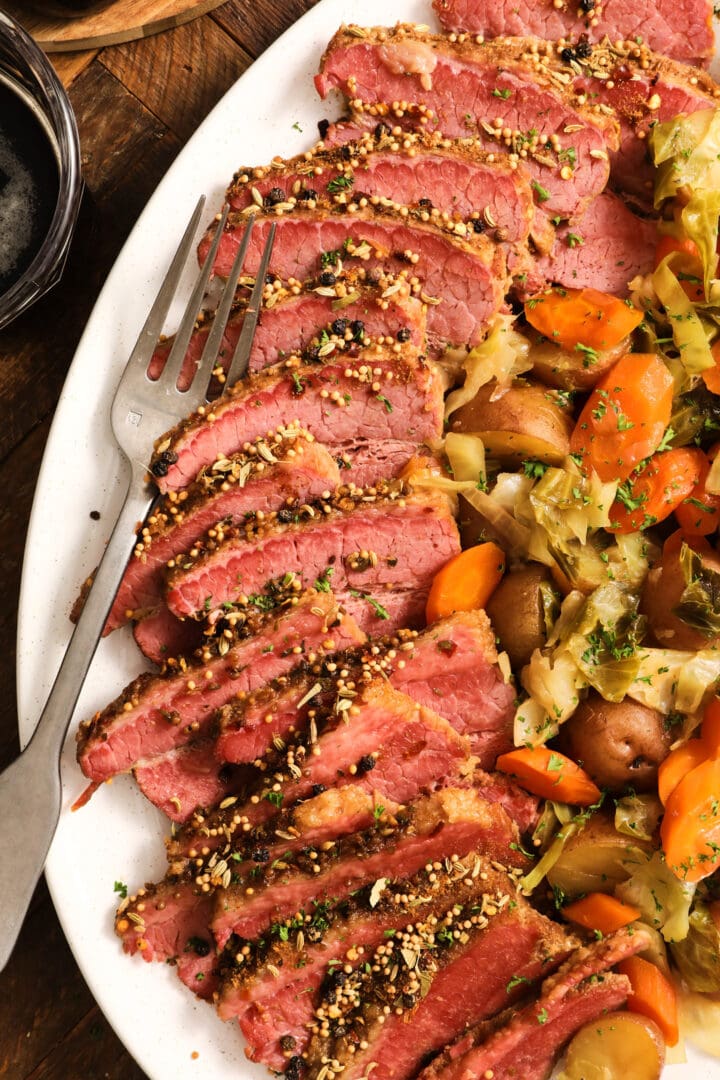 white platter with slices of corned beef brisket and vegetables, including cabbage, carrots and potatoes.