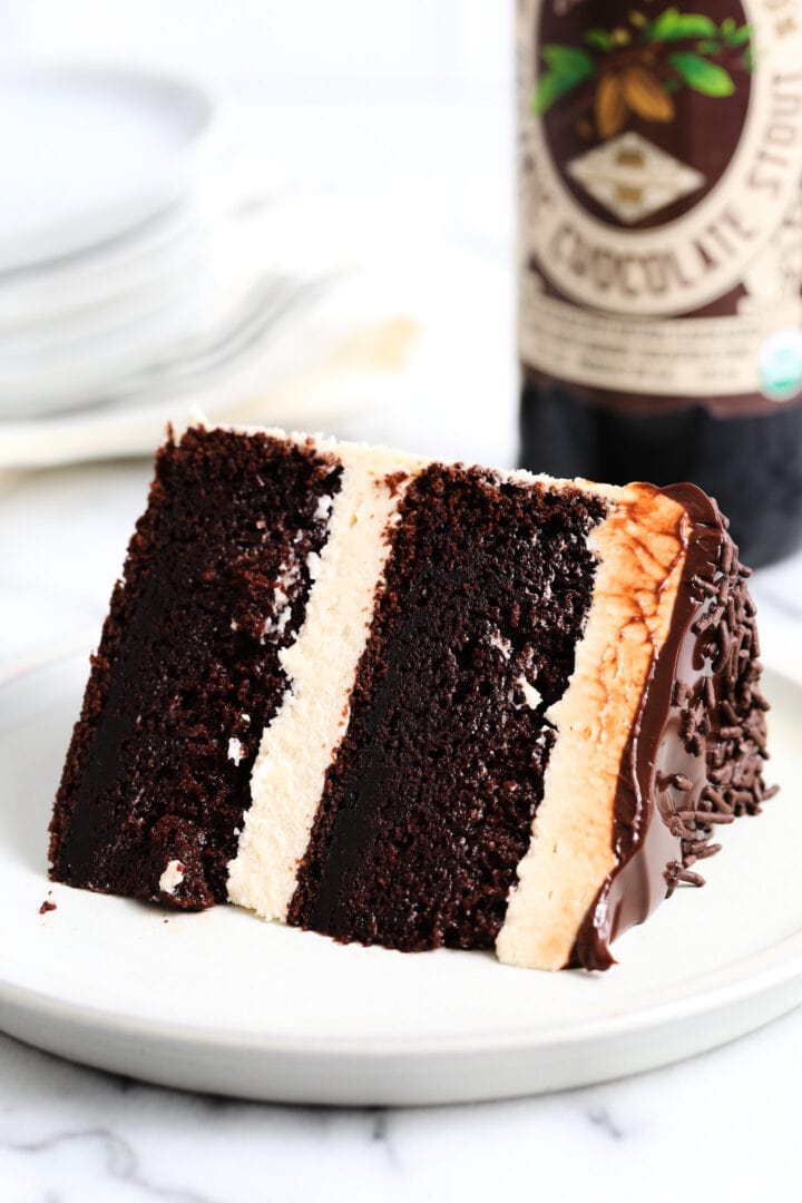 slice of chocolate stout cake with tan Irish buttercream, chocolate ganache and sprinkles. There is a beer bottle in the background.