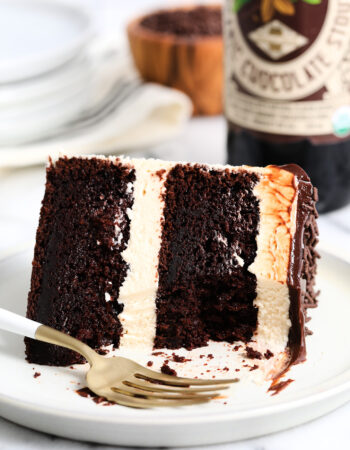 slice of chocolate stout cake with tan Irish buttercream, chocolate ganache and sprinkles. There is a beer bottle in the background.