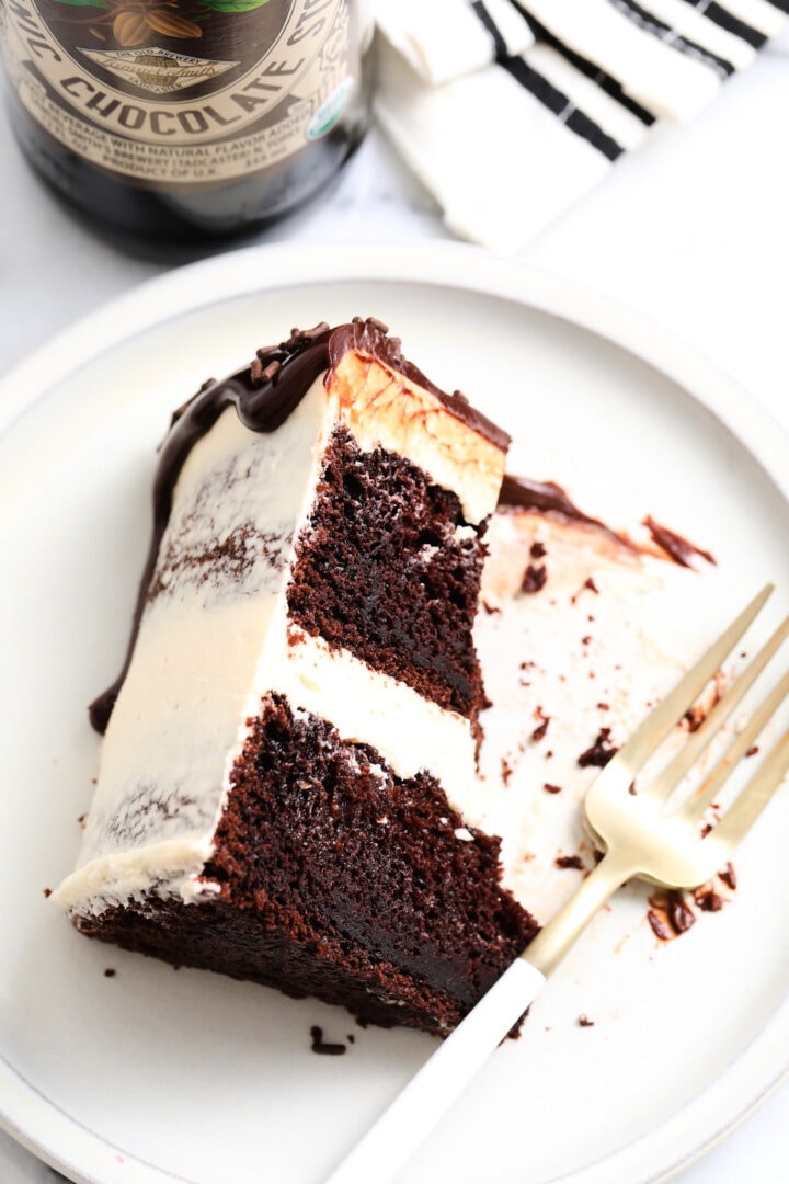 slice of chocolate stout cake with tan Irish buttercream, chocolate ganache and sprinkles. There is a beer bottle in the background.