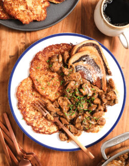 plate of potato pancakes, mushroom gravy and chives on a white plate with a cup of coffee to the right.