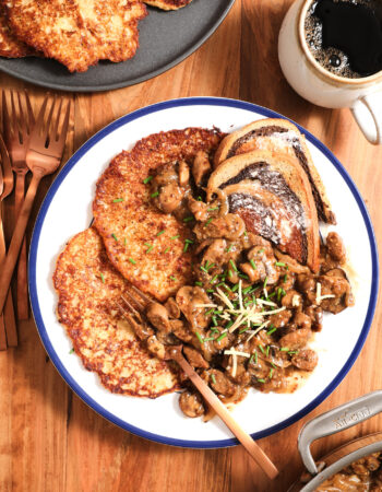 plate of potato pancakes, mushroom gravy and chives on a white plate with a cup of coffee to the right.