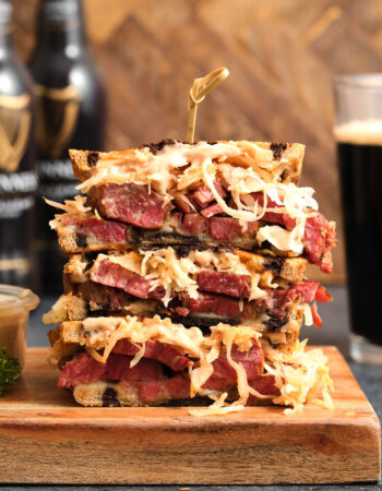 reuben sandwich with sauerkraut, beef, russian dressing and swiss cheese. There are bottles of beer in the background.