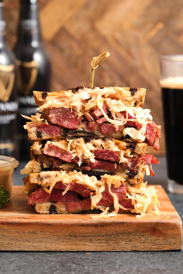 reuben sandwich with sauerkraut, beef, russian dressing and swiss cheese. There are bottles of beer in the background.