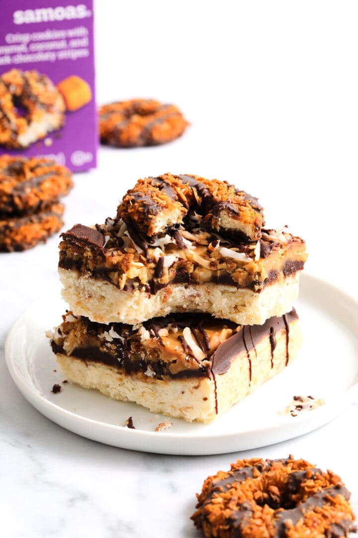 two shortbread cookie bars topped with chocolate, caramel and toasted coconut flakes. There are several other round cookies in the background.