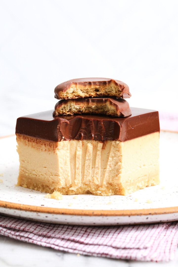 one peanut butter cheesecake bar on a white speckled plate with a bite taken out, and two cookies stacked on top.