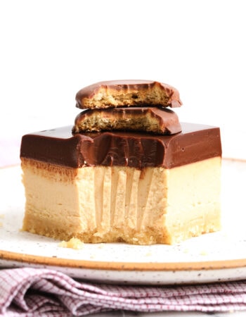 one peanut butter cheesecake bar on a white speckled plate with a bite taken out, and two cookies stacked on top.