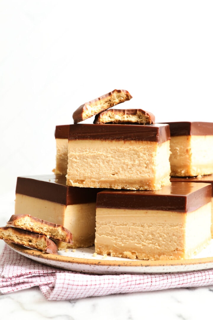 stack of peanut butter cheesecake bars on a white speckled plate.