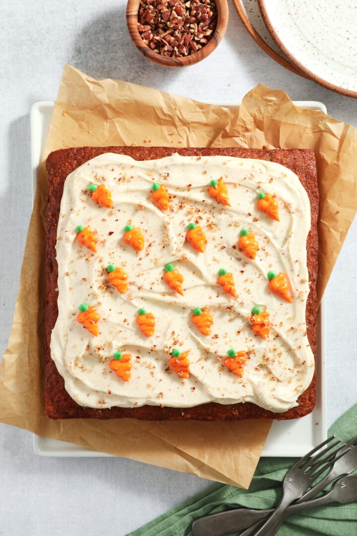 full carrot cake with white cream cheese frosting and small carrots piped onto the top.
