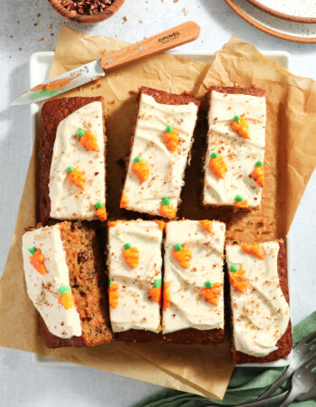 carrot cake that has been cut into eight pieces, with plates off to the side and forks on the lower right hand corner.