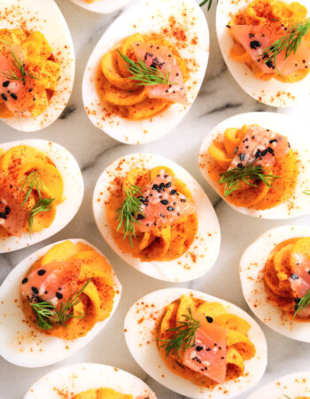 top view of smoked deviled eggs with a sprinkle of paprika, fresh dill, smoked salmon, and poppy seeds.