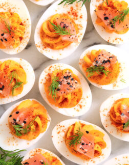 top view of smoked deviled eggs with a sprinkle of paprika, fresh dill, smoked salmon, and poppy seeds.