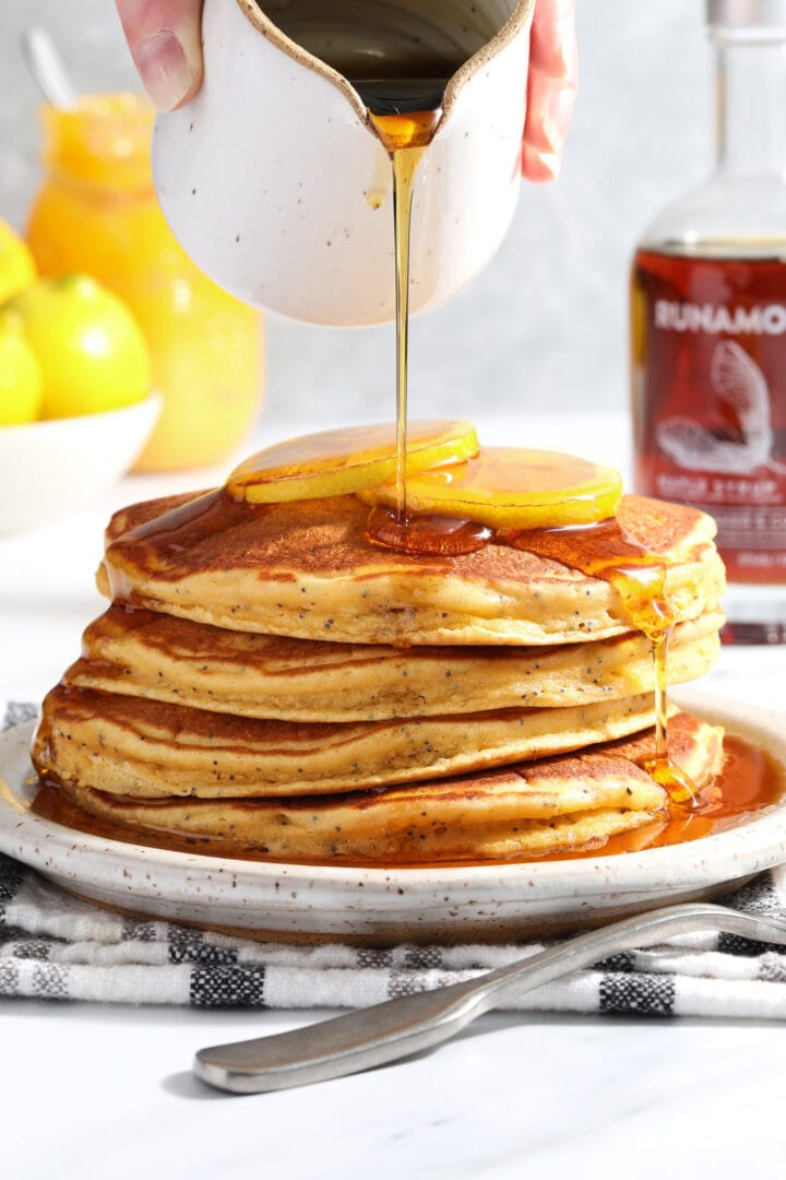 stack of lemon poppyseed pancakes being drizzled with syrup.