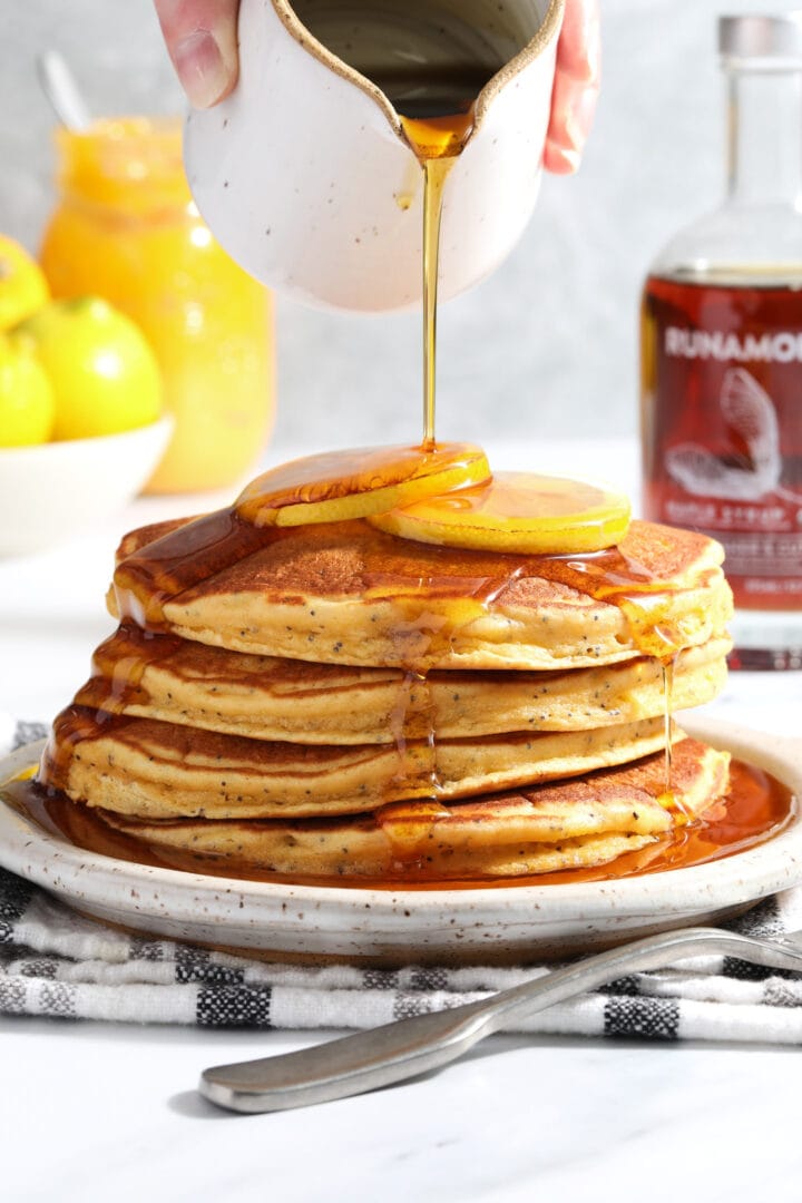 stack of lemon poppyseed pancakes being drizzled with syrup.