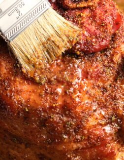 a whole ham being brushed with a maple mustard glaze.