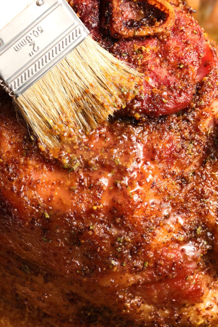 a whole ham being brushed with a maple mustard glaze.