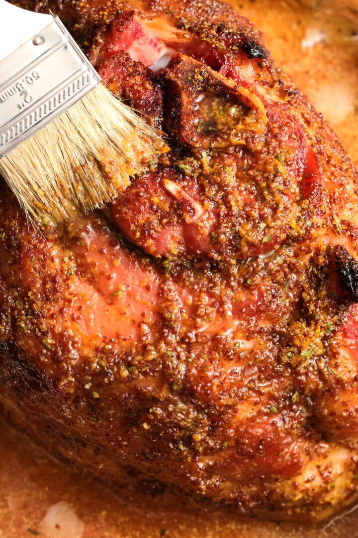 a whole ham being brushed with a maple mustard glaze.