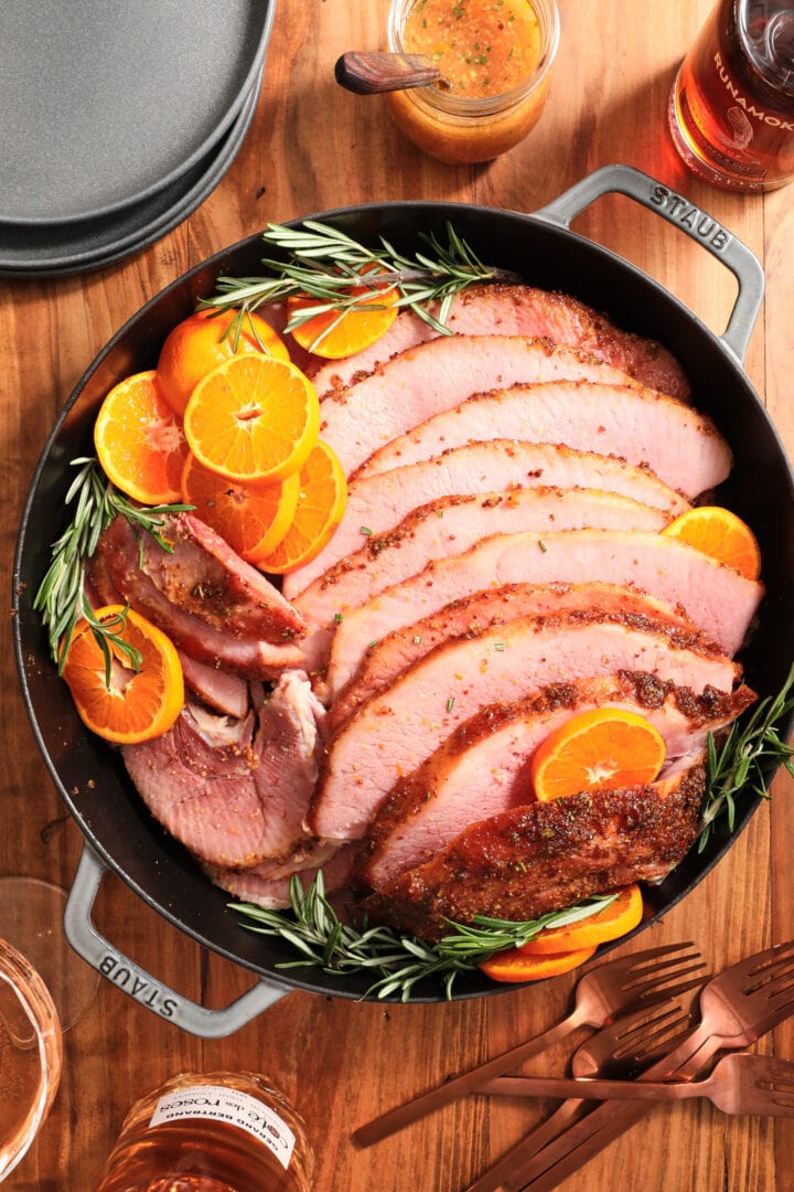 large gray skillet with ham slices arranged with cut oranges and fresh rosemary sprigs.