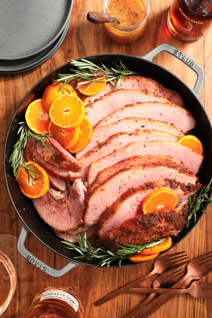 large gray skillet with ham slices arranged with cut oranges and fresh rosemary sprigs.