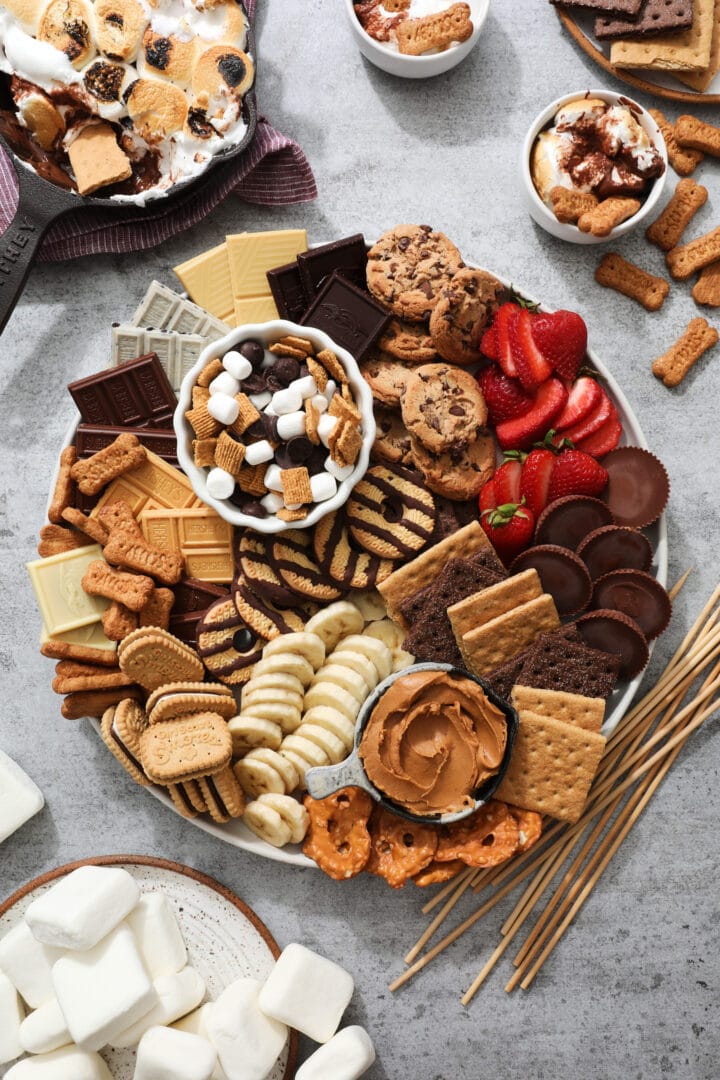 s'mores snacking tray, that includes chocolate chip cookies, graham crackers, sliced strawberries, sliced bananas, marshmallows, candy and chocolate bars.