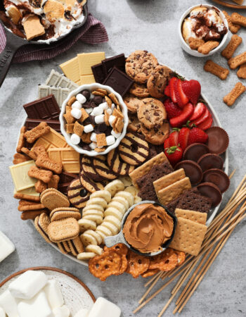 s'mores snacking tray, that includes chocolate chip cookies, graham crackers, sliced strawberries, sliced bananas, marshmallows, candy and chocolate bars.