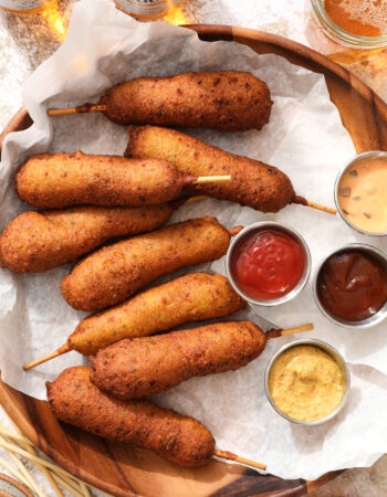 tray of jalapeno cheddar corn dogs with different dipping sauces and a few bottles of beer in the top left hand corner of the picture.