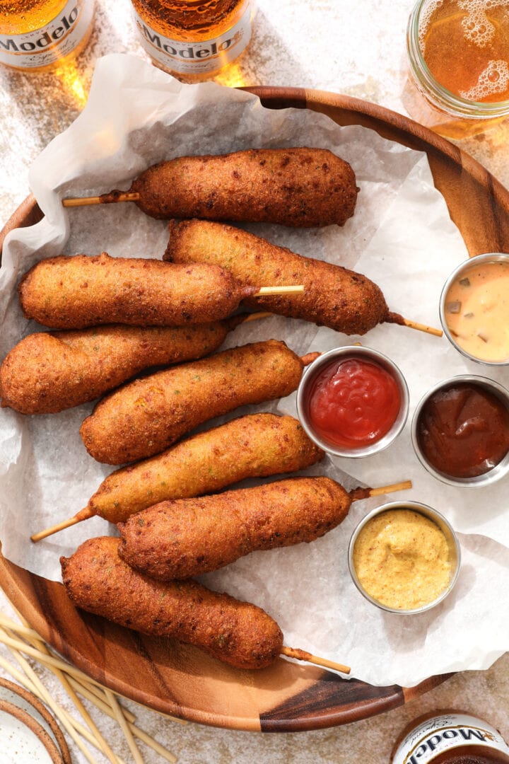 tray of jalapeno cheddar corn dogs with different dipping sauces and a few bottles of beer in the top left hand corner of the picture.