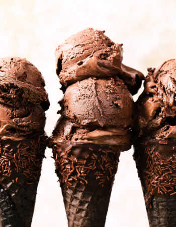 three chocolate ice cream cones dipped in chocolate and sprinkles, with two scoops of chocolate ice cream on each cone.