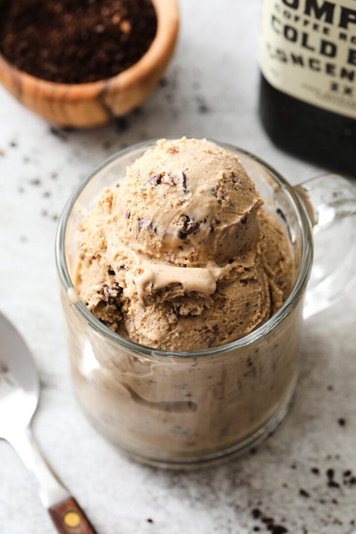 clear coffee mug with several scoops of coffee ice cream. There is a small bowl of coffee grounds off to the left.