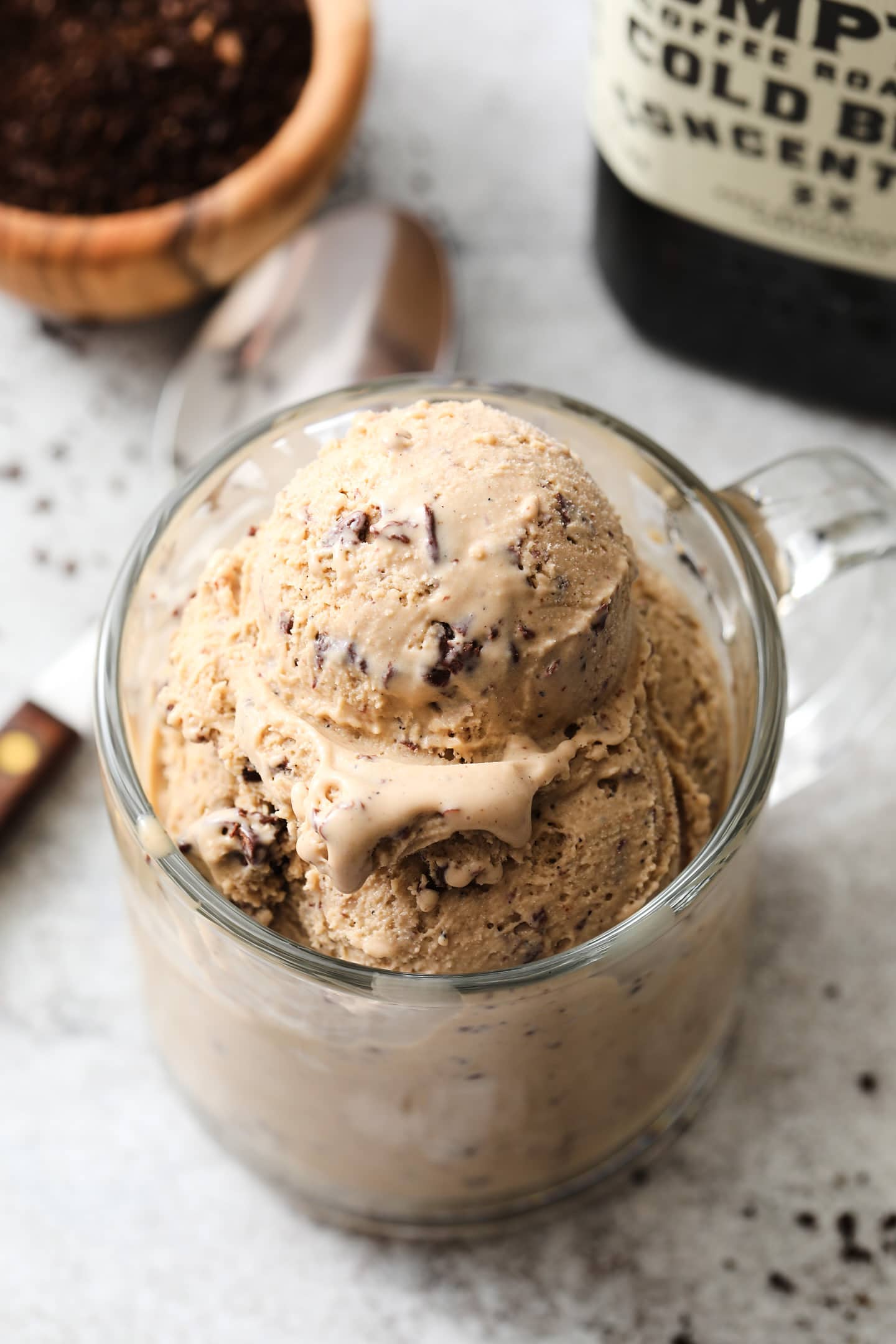 clear coffee mug with several scoops of coffee ice cream. There is a small bowl of coffee grounds off to the left.