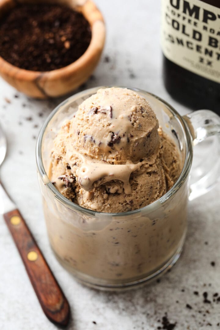 clear coffee mug with several scoops of coffee ice cream. There is a small bowl of coffee grounds off to the left.