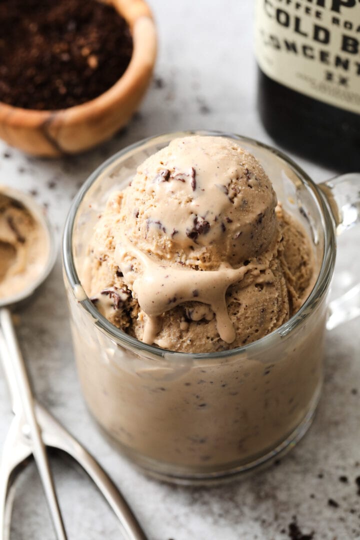 clear coffee mug with several scoops of coffee ice cream. There is a small bowl of coffee grounds off to the left.