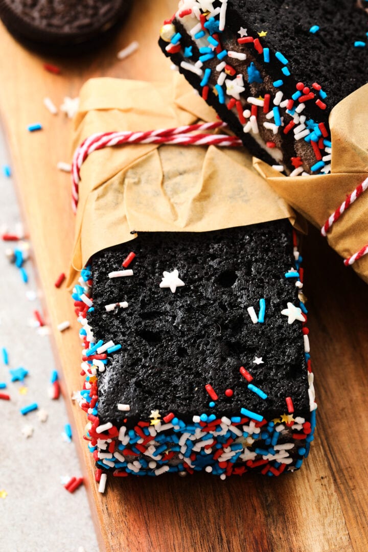 chocolate sandwich cookie ice cream bars, decorated with red, white and blue sprinkles and wrapped in brown parchment paper.