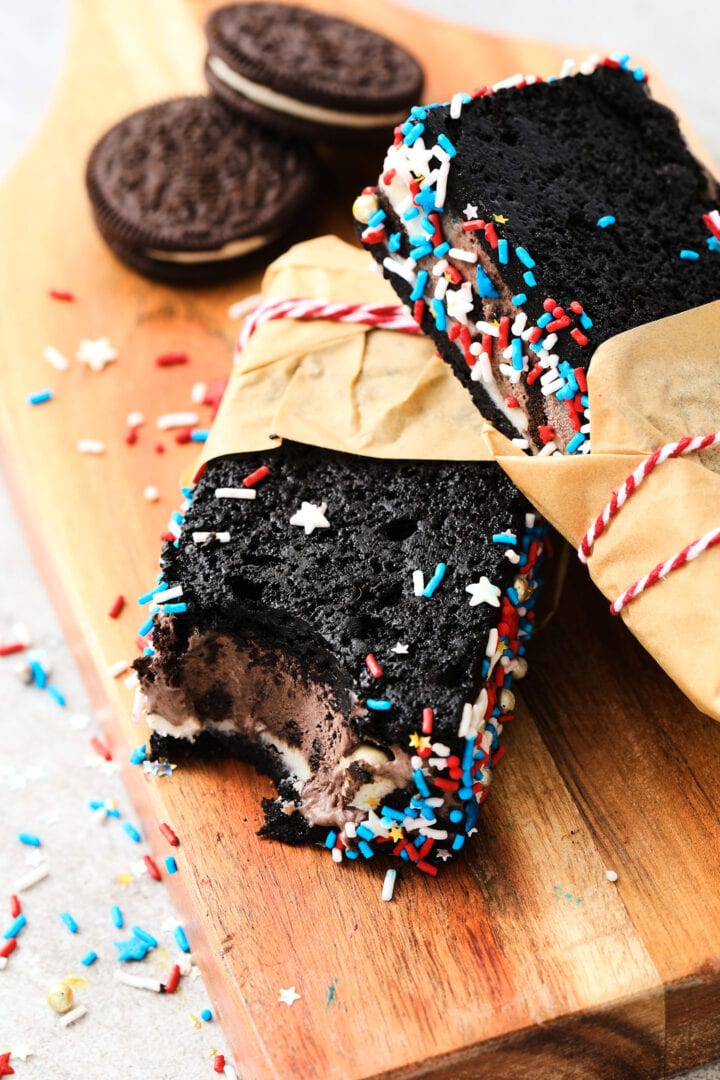 chocolate sandwich cookie ice cream bars, decorated with red, white and blue sprinkles and wrapped in brown parchment paper.