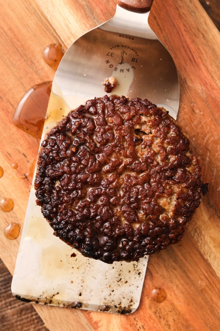 a fresh beef burger patty on a metal spatula.