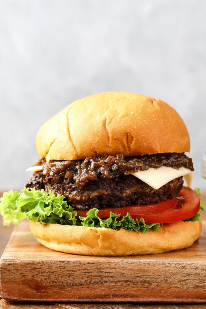 cheeseburger with caramelized onions and a slice of white cheese. There is a slice of lettuce and a few slices of tomatoes on the bottom of the burger.