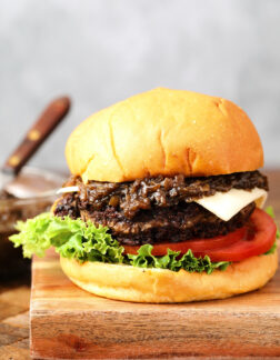 cheeseburger with caramelized onions and a slice of white cheese. There is a slice of lettuce and a few slices of tomatoes on the bottom of the burger.